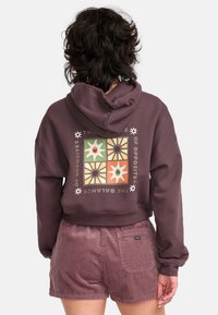 Purple cropped hoodie with a floral graphic design on the back, paired with textured pink corduroy shorts featuring a back pocket.