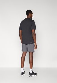 Μαύρο κοντομάνικο μπλουζάκι συνδυασμένο με γκρι σορτς, κατασκευασμένο από ελαφρύ ύφασμα. Το σύνολο ολοκληρώνεται με μαύρα αθλητικά παπούτσια και λευκές κάλτσες.