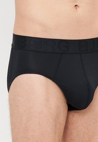 Černé bavlněné kalhotky s širokým elastickým pasem, na kterém je v kontrastní černé barvě embosovaný nápis "BJORG". Materiál má jemnou texturu a přiléhavý střih.