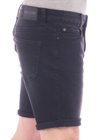 Pantalones cortos de mezclilla negra con puños enrollados, cinco bolsillos y un parche de cuero de la marca en la cintura. Textura suave, ajuste Slim, diseño casual.