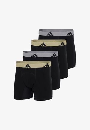 Atletisk mand står barfodet iført sorte boksershorts med en lys farvet talje, der har Adidas-logoer, og kigger mod højre.