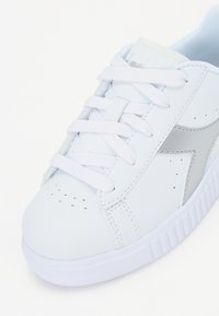Sneaker bianca in pelle con accenti argento, punta rotonda, perforazioni e lacci bianchi. Presenta una suola testurizzata e un interno imbottito.