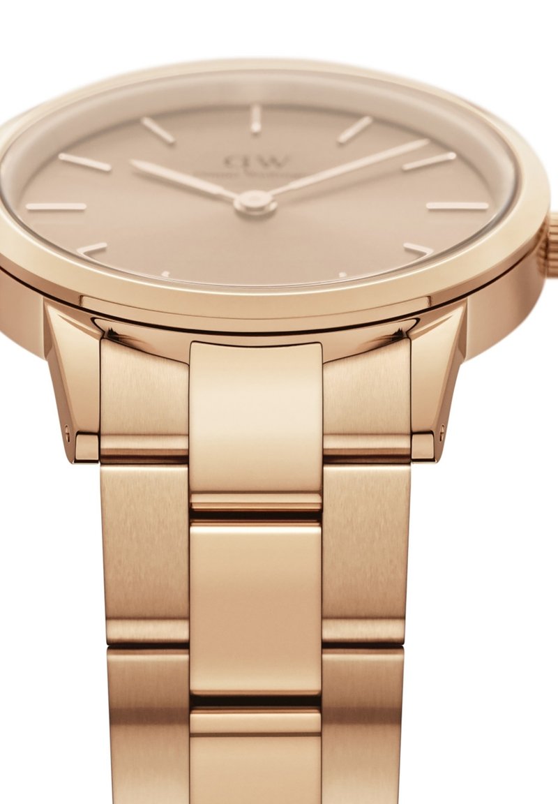 Montre en or rose avec un boîtier lisse et rond, un cadran minimaliste avec des index horaires, et un bracelet en métal brossé avec des accents polis.