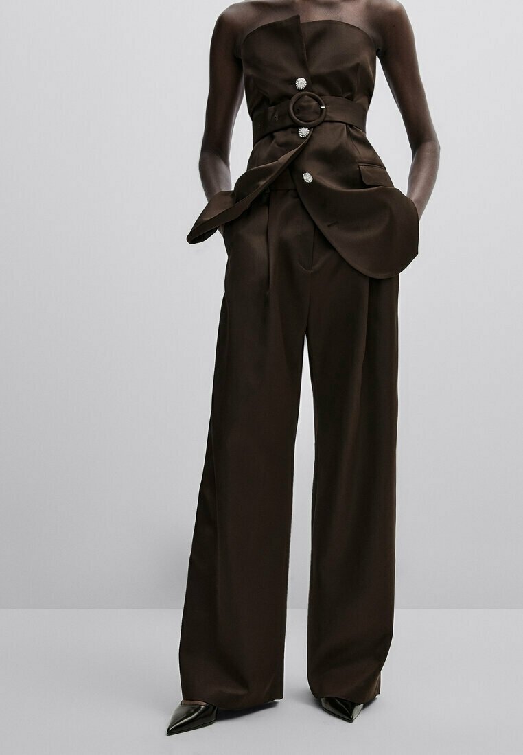 Combinaison-pantalon bustier marron foncé à jambes larges, avec une large ceinture, trois boutons décoratifs, des poches et des chaussures noires pointues.