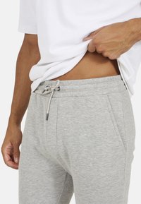 Szare spodnie dresowe z elastycznym pasem, zaciąganym sznurkiem i bocznymi kieszeniami. Miękka, teksturowana tkanina z delikatnym melanżowym wzorem.