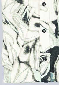 Blumengemusterte Stofftasche mit hellgrünen und schwarzen Wirbeln auf einem crèmefarbenen Hintergrund, gesichert mit zwei schwarzen Knöpfen.