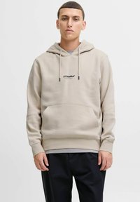 Beige Kapuzenpullover mit Kordeln, Vordertasche und schwarzem Logo "JJ Studios" auf der Brust. Hergestellt aus einem weichen, strukturierten Stoff mit gerippten Bündchen.
