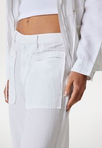 Vita bomullbyxor med stora fickor, elegant design och avslappnad passform, matchade med en vit ribbad crop top och en ljus jacka.
