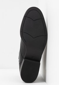 Semelle de chaussure noire avec une surface texturée et un motif, ainsi que des rainures discrètes. La taille "37" est indiquée sur le côté de la semelle.