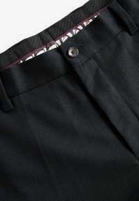 Pantalons noirs texturés avec une fermeture à bouton et une ceinture intérieure à motif. Le tissu présente un tissage raffiné et une construction robuste.