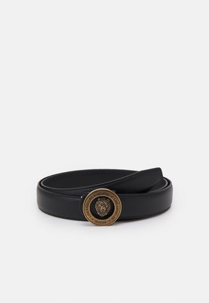 Ceinture en cuir noir enroulée, avec une boucle ronde dorée ornée d'une tête de lion et gravée de l'inscription "GUESS LOS ANGELES".