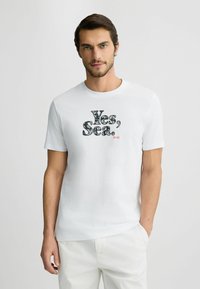 Hvid bomulds T-shirt med teksten "Ja, Hav." i et dekorativt print og et lille rødt logo, korte ærmer og design med rund hals.