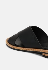 Sandale en cuir noir avec une semelle en liège et un design à bout ouvert, présentant une texture lisse et un détail de branding minimaliste.