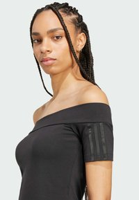 Musta olkapäiltä avonainen paita, joka on valmistettu sileästä kankaasta. Paitassa on lyhyet hihat, joissa on kiiltäviä kolmiraitakoristeita vasemmalla olkapäällä.