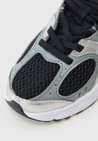 Baskets de sport noires et grises avec une tige en mesh, accents argentés et détails texturés sur le bout et les côtés. Les lacets sont noirs.
