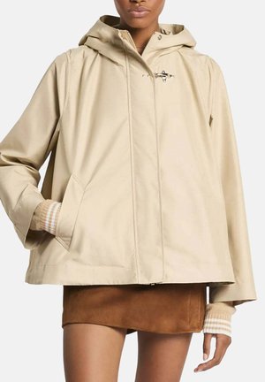 Veste beige à capuche avec poches avant portée sur une mini-jupe en daim marron et des poignets tricotés rayés.