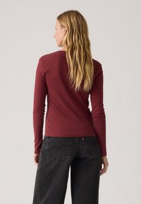 Burgunderfarget langermet skjorte med en tettsittende design, laget av mykt materiale. Brukt sammen med mørkegrå vide jeans, som viser en uformell stil.