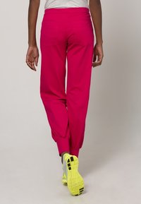 Roze joggingbroek met elastische boorden, gemaakt van een gladde stof, met twee achterzakken en een hoge tailleband, gecombineerd met felgele sportschoenen.