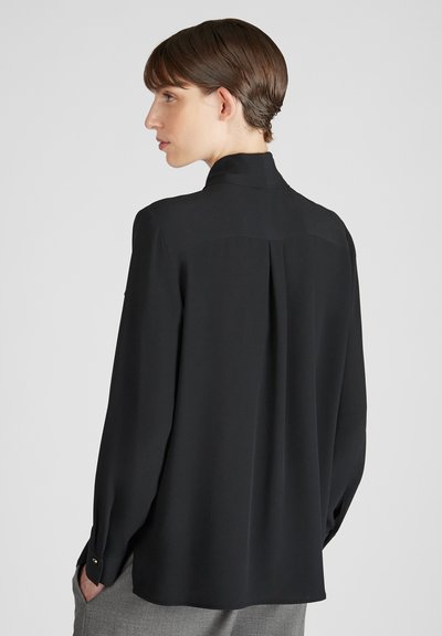 Camicetta nera a maniche lunghe realizzata in materiale leggero con colletto alto, piega sul retro e polsini con bottoni. Texture liscia e design minimalista.