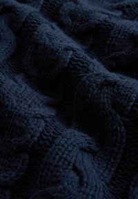 Marineblauwe gebreide textiel met een kabelpatroon, dat een zachte textuur en variërende steektechnieken in een golvende structuur toont.