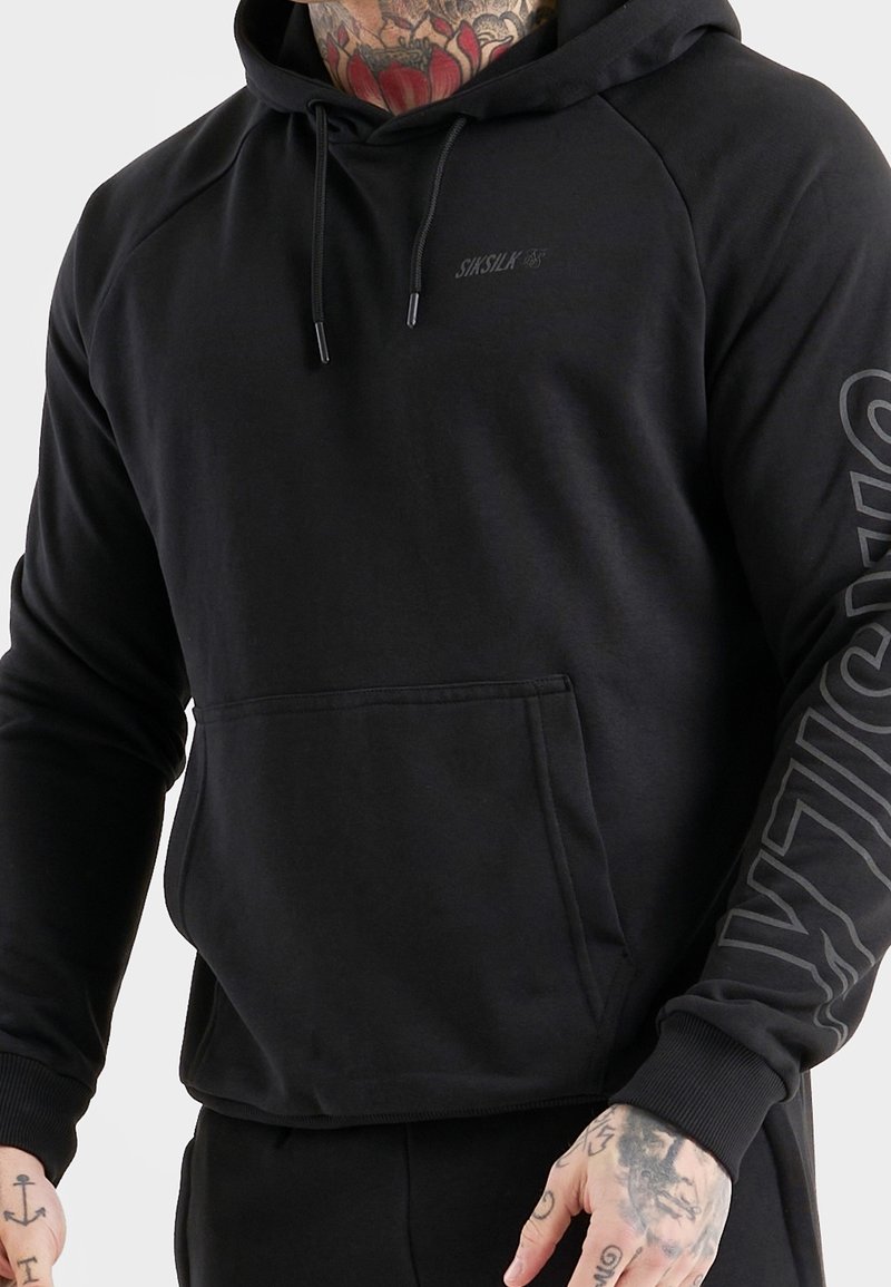 Sweat-shirt noir à capuche avec une poche kangourou, des poignets côtelés et un logo imprimé sur la manche. Tissu lisse avec une finition mate.
