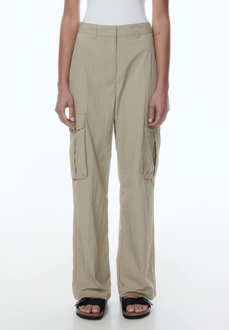 Beige cargobroek met een relaxte pasvorm, voorzien van zijzakken en een gladde, lichte stof. G gedragen met zwarte sandalen.