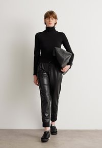 Black turtleneck sweater paired with fitted black leather joggers and black sneakers. The model carries a black clutch.