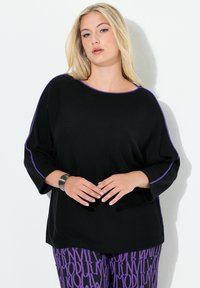 Czarny dzianinowy top z fioletowym akcentem wokół dekoltu i rękawów, o luźnym kroju i rękawach do łokcia. W połączeniu z fioletowymi spodniami w wzory.