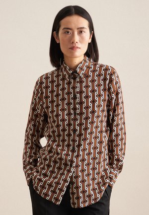 Chemise à boutons avec un motif de chaîne géométrique dans des tons de marron, blanc et orange. Fabriquée en tissu lisse, avec un col et des manches longues.