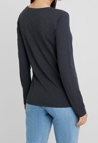 Mörkgrå långärmad t-shirt, lättviktig, med rundad halsringning och figursydd design, tillsammans med ljusblå denimjeans.