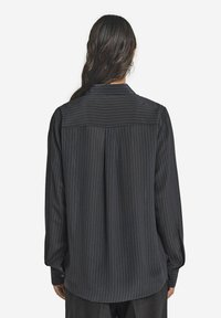 Svart långärmad skjorta med vertikala ränder, med en avslappnad passform, knäppningar i ärmsluten och en ryggsömdesign. Slät textur.
