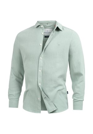 Camicia lunga a maniche verdi chiaro realizzata in tessuto texturizzato, con colletto button-down, bottoni frontali e un piccolo logo sul petto.