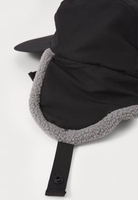 Svart utendørs hatt med en grå, lodden foring og stiv skjerm. Har justerbar stropp med knappelukking og myk teksturert stoff.