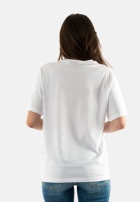 Camiseta de algodón blanca de manga corta, con escote redondo y corte relajado. Se lleva con vaqueros azules, mostrando la vista trasera. Sin patrones ni gráficos.