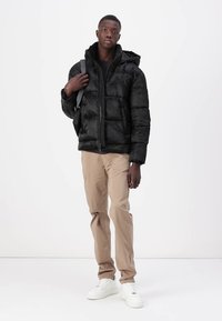 Melns pūkains jaka ar kapuci, ar izšūtu tekstūru un priekšējo rāvējslēdzēju. Apvienota ar beidža biksēm un baltām kedām.