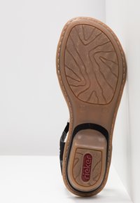 Black sandal with textured rubber sole, featuring a light brown base and embossed tread pattern. Rieker logo in red prominently displayed.