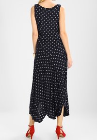 Navy blue sleeveless maxi dress with small white floral pattern, side slits, and flowy fabric. Worn with red heels.