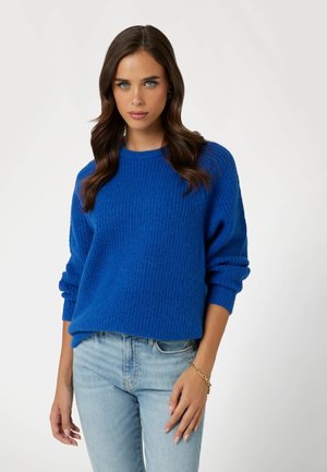 Blauer, gestrickter Pullover mit gerippter Textur, rundem Ausschnitt und lockeren Ärmeln, kombiniert mit hellblauen Jeans.