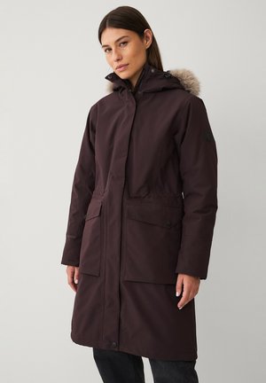 Bordeaux lange parka-jack met een faux fur-voering in de capuchon, twee voorzakken en een gladde stoftextuur. Voorzien van drukknopen.
