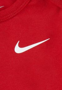 Tricou roșu din bumbac, cu decolteu rotund, având un logo Nike swoosh alb proeminent în față. Textură netedă, croială clasică.