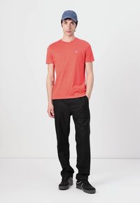 Tricou scurt roșu cu guler rotund, asortat cu pantaloni negri și adidași negri. Pălăria este albastră, cu o margine curbată.