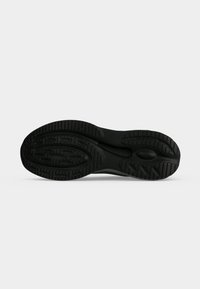 Semelle de chaussure en caoutchouc noir avec des motifs de bandes de roulement conçus pour l'adhérence, présentée sur un fond clair uni.