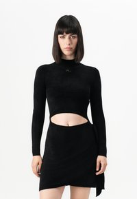 Čierny dlhý rukáv crop top s vysokým golierom a výrezovým dizajnom, v kombinácii s odpovedajúcou obálkovou sukňou, vyrobený z mäkkej textúrovanej látky.