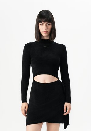Zwarte lange mouwen crop top met een opstaande kraag en uitsnijdingen, gecombineerd met een bijpassende wikkelrok, gemaakt van een zachte, gestructureerde stof.