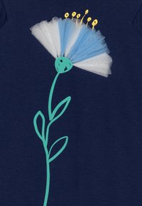 Námořnická látka má modro-bílý květinový vzor se zeleným stonkem a listy, doplněný o žluté tyčinky na vrcholu.