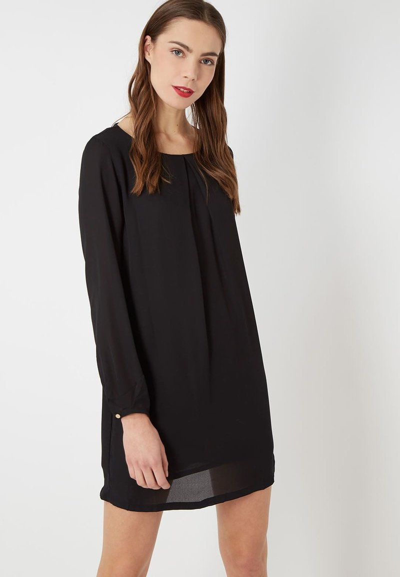 Vestido negro de manga larga en tejido ligero con un corte relajado, escote redondeado y sutiles detalles plisados en la parte frontal.