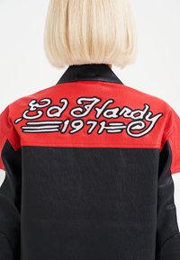 Black and red leather jacket featuring white embroidered text "Ed Hardy 1971" on the back, with a sleek, textured finish and contrasting collar.