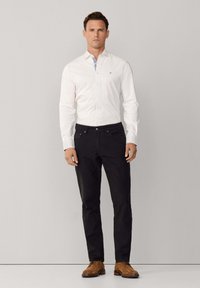 Witte blouse met lange mouwen en een blauw ruitpatroon aan de binnenkant van de kraag, gecombineerd met zwarte broek en bruine leren schoenen. Eenvoudig ontwerp en pasvorm.