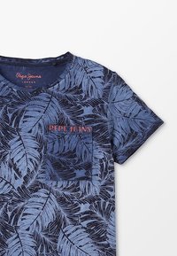 Granatowy T-shirt z wzorami liści, okrągły dekolt, krótkie rękawy i kieszonka na lewym piersi. Logo marki w kontrastowym czerwonym tekście.