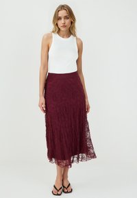 Jupe midi en dentelle bordeaux avec un motif floral, dotée d'une taille ajustée et d'une silhouette fluide. Associée à un haut sans manches blanc.